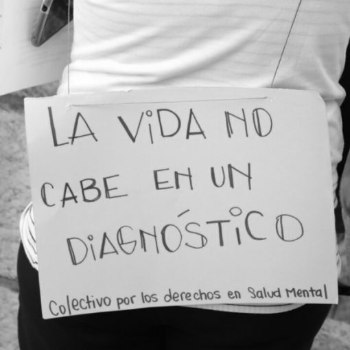 Foto Marcha por el Derecho a la Salud Mental. Se ve a una persona en la movilización, en sus espaldas un cartel que dice "la vida no cabe en un diagnóstico"