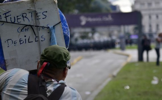 Foto de una mujer de espaldas sosteniendo un cartel en una manifestación. En el cartel se lee: "Fuertes con los débiles". Fuente: tapa del libro.